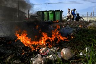 Cette photo montre des personnes circulant à moto devant des déchets plastiques en feu en périphérie de Phnom Penh. © Tang Chhin Sothy / AFP